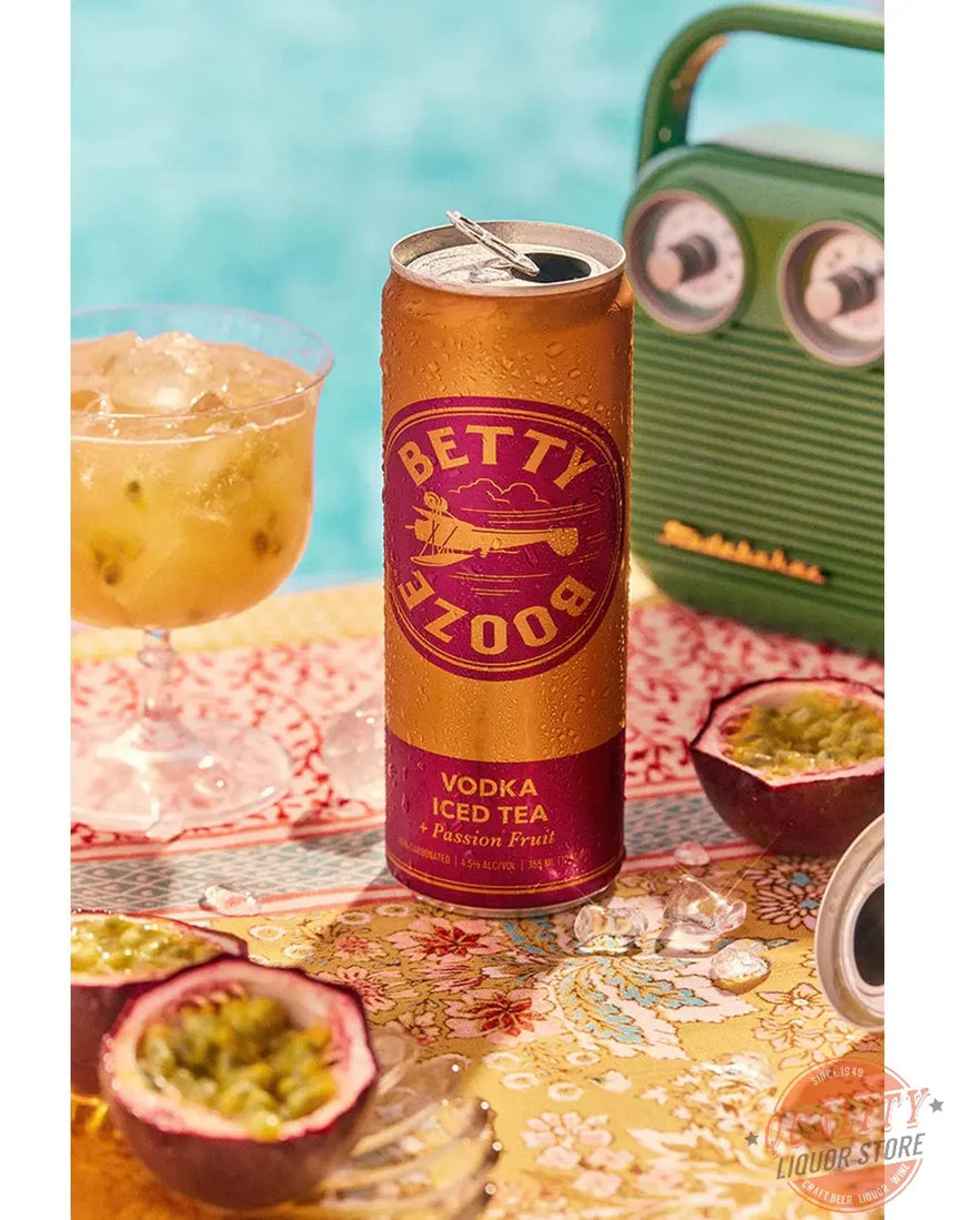 Can of Betty Booze Vodka Iced Tea with Passion Fruit on a table with a cocktail and fruit.