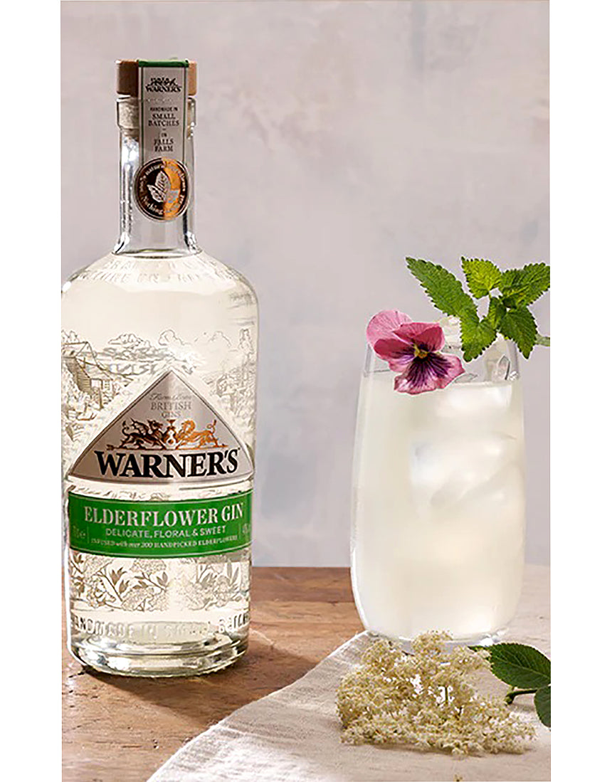 Warner's Elderflower Gin bottle with a cocktail garnished with flowers on a wooden surface.