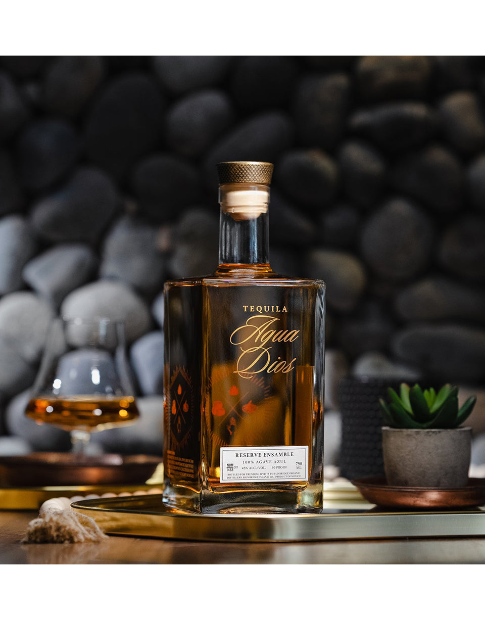 Tequila bottle labeled 'Agua Dios' on a wooden surface with a blurred stone wall background