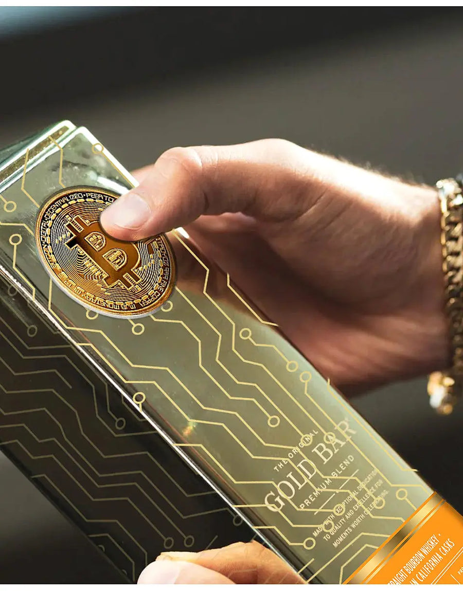 Hand holding a clear container with a gold coin featuring a Bitcoin design, branded 'The Gold Bar'.