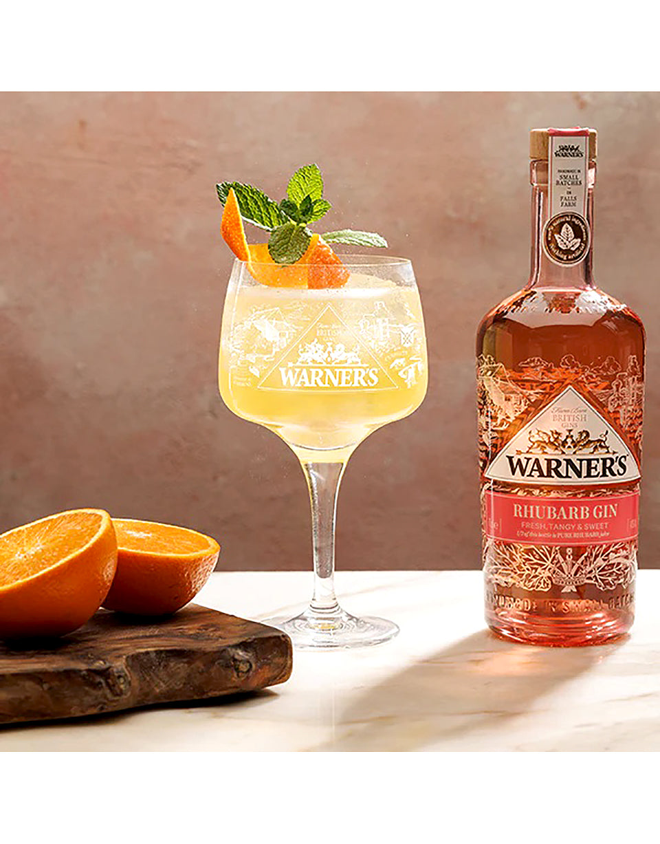 Warner's Rhubarb Gin bottle with a cocktail and oranges on a wooden board.